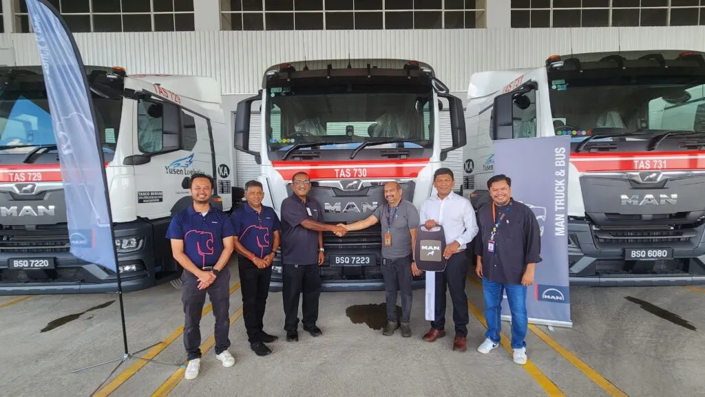 Representatives from MAN Truck & Bus Malaysia and TASCO Berhad shaking hands while holding a large ceremonial key in front of three white Euro V MAN TGS 6x2 prime movers. (Photo: MAN Malaysia)