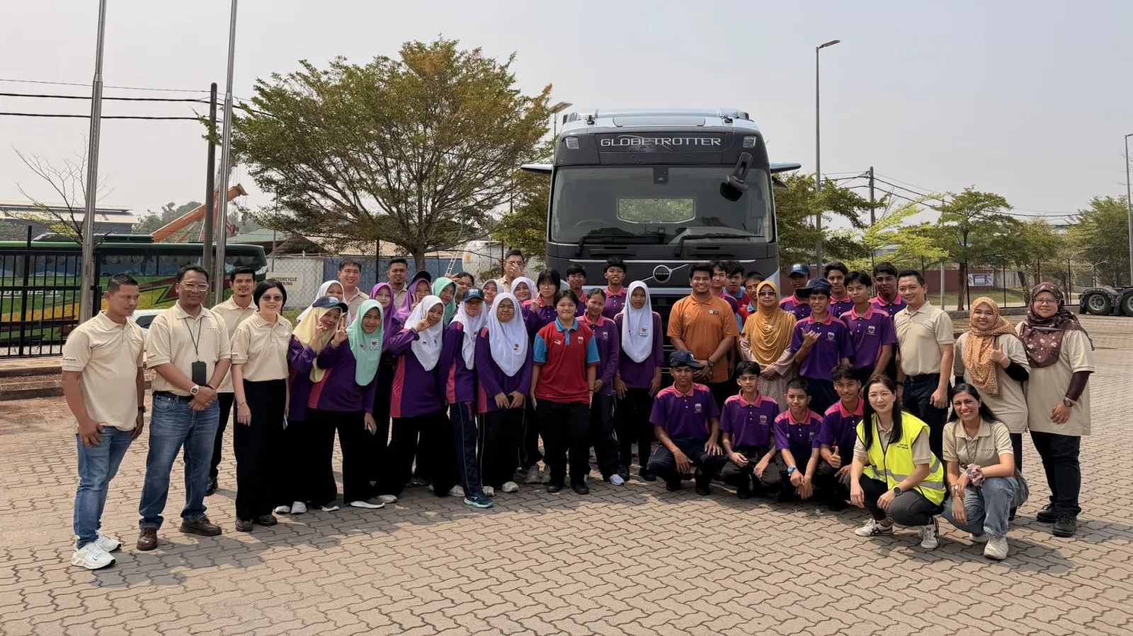 A large group of students and facilitators posing together in front of a heavy-duty Volvo Globetrotter truck outdoors at a service dealership lot.