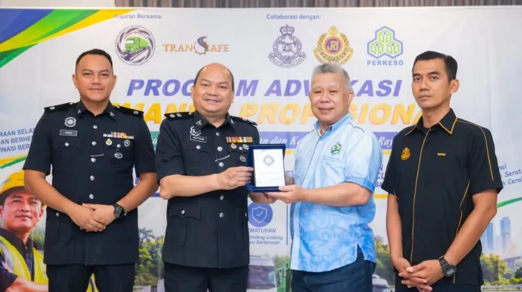Four male officials in uniform and corporate attire posing together on stage during a souvenir presentation ceremony at the Professional Driver Advocacy Programme backdrop.