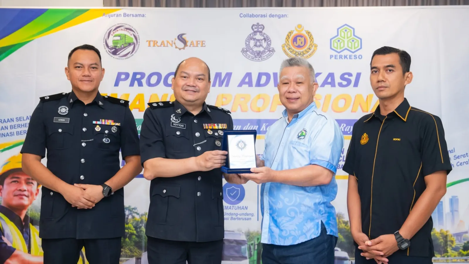 Four male officials in uniform and corporate attire posing together on stage during a souvenir presentation ceremony at the Professional Driver Advocacy Programme backdrop.