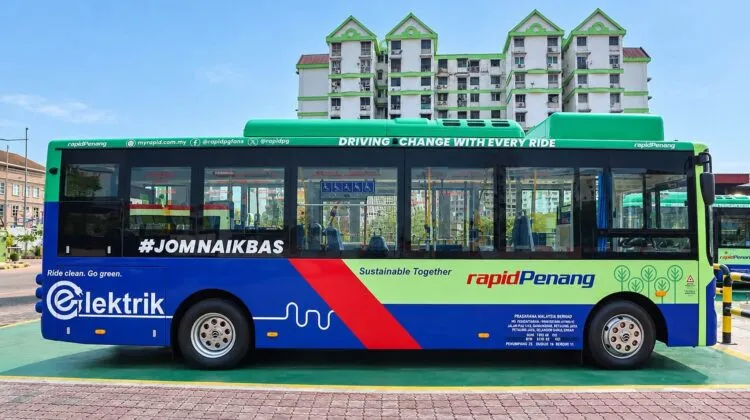 Side view of a green and blue Rapid Penang electric transit bus with green "Elektrik" branding on the side panel, parked outdoors in front of a residential building.