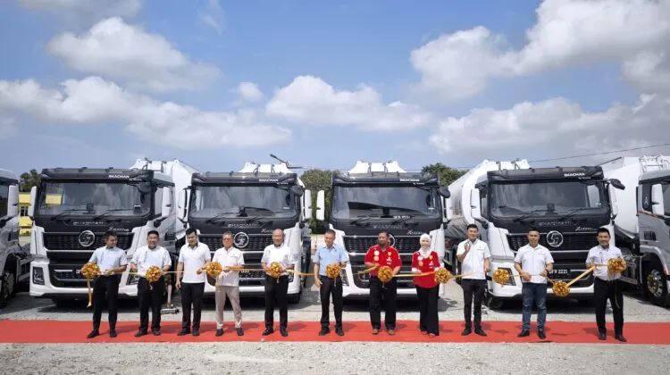 A lineup of company executives and guests holding a golden ribbon across a red carpet in front of four white Shacman X5000 Pro prime mover trucks parked outdoors.